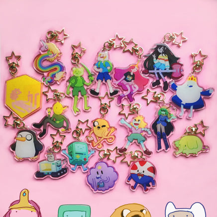A collection of colorful character acrylic keychains with gold-tone star clips, arranged on a solid pink background.