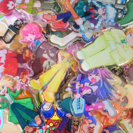 A pile of colorful anime character acrylic keychains and charms with attached metal key rings, photographed close up on a light surface.