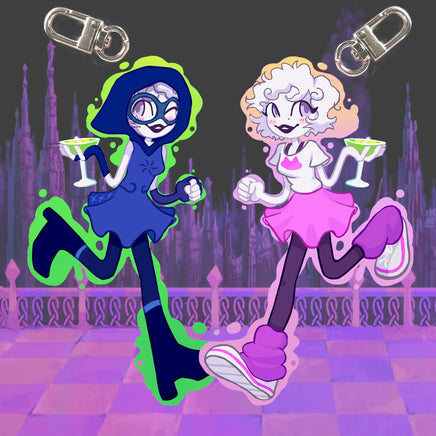 Two cartoon-style acrylic keychain charms with metal swivel clips, shown against a dark illustrated cityscape background. The left charm depicts a blue-haired character in a blue dress with green slime accents and a martini glass.