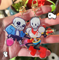 Two cartoon skeleton keychains held in a hand with a blurred background